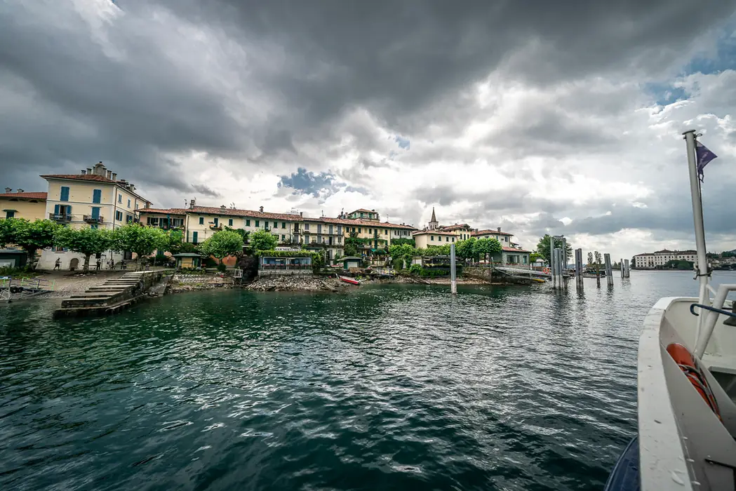 Blick vom Boot auf den Ort am Lago Maggiore unter wolkigem Himmel