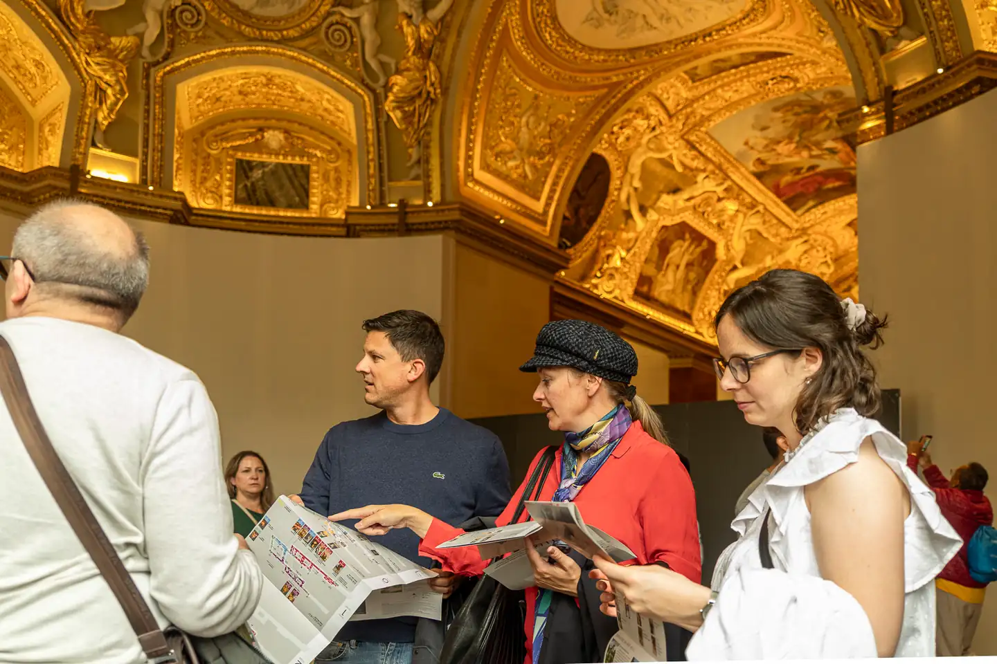 Teammitglieder mit Museumsplänen unter einer verzierten Decke im Louvre